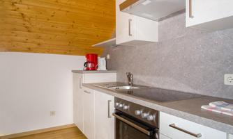 A modern kitchen with white cabinets and a wooden ceiling. The kitchen is well equipped with a stove and a range hood.