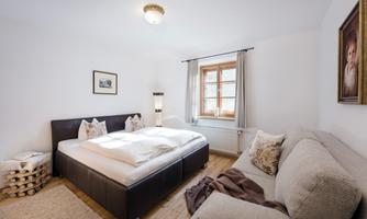 A bright bedroom with a double bed and a cozy sofa. Large windows provide plenty of daylight and a pleasant atmosphere.