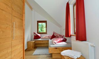 A cozy room with wooden furniture and red curtains. The windows offer a view of the greenery.