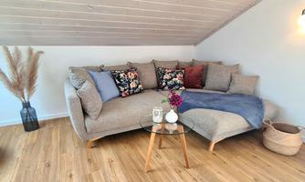 A cozy couch with colorful cushions is in a bright room. Next to the couch is a small table with a vase and a plant.