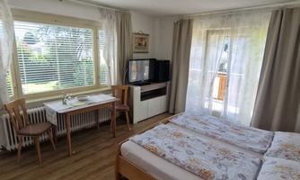 A cozy bedroom with two beds and a table. Large windows let in plenty of light and offer a view of the greenery.