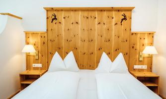 A cozy bedroom with a wooden headboard and two light pillows. On the walls, there are modern lamps and wooden shelves.