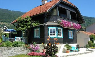 A pretty black wooden house with a red-tiled roof. Colorful flowers and plants adorn the garden and the facade.