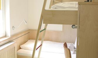 A simple room with a loft bed and a single bed. There is a wooden staircase and a chair in the room.