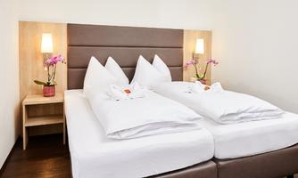 A cozy bedroom with a double bed and white bedcovers. Next to the bed, there are nightstands decorated with flowers.