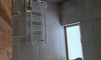 A modern bathroom with gray tiles and a towel holder. A large window lets natural light in.