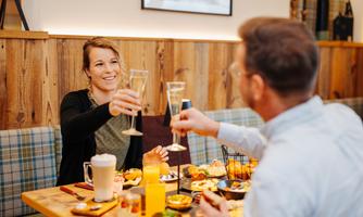 A cozy meal with friends. Two people toast with glasses, surrounded by delicious food.