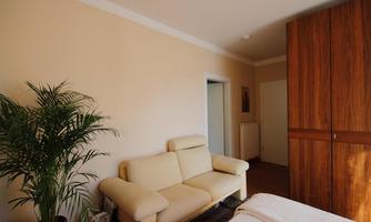 A cozy room with a beige sofa and a large wooden wardrobe. A green plant complements the warm atmosphere of the room.