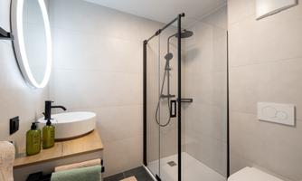A modern bathroom with a walk-in shower and a round mirror. On the sink, there are green toiletries and towels.