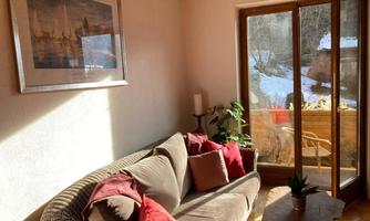 A cozy living room with a comfortable sofa and colorful cushions. Large windows let in plenty of daylight and offer a view of the snowy landscape outside.