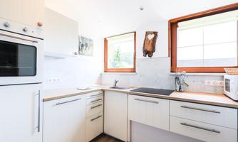 A modern kitchen with white cabinets and wooden countertops. Large windows provide plenty of daylight.