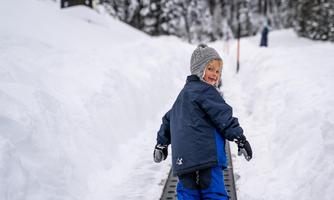 A happy child walks on a snow-covered path. In the background, snow-covered trees and houses can be seen.
