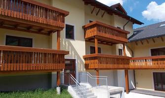 A modern building with wooden balconies and large windows. The outdoor area is designed with grass and access to the entrance.