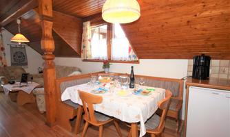 A cozy attic apartment with a dining area and a small kitchen. The table is set for a meal, and the wooden paneling creates a warm atmosphere.