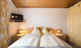 A cozy bedroom with two beds and a wooden ceiling. A TV and bedside lamps create a homely atmosphere.