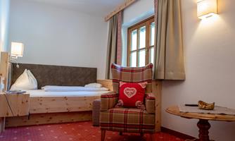 A cozy room with a double bed and a comfortable armchair. Decorated with warm colors and wooden details, it offers an inviting atmosphere.