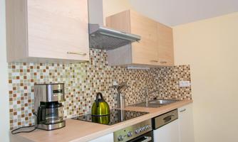 A modern kitchen unit with light cabinets and a mosaic tile. The kitchen is equipped with a stove, a sink, and a coffee machine.