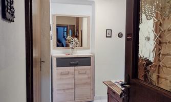 A bright hallway with a modern sideboard and a mirror. Some pictures hang on the wall, and a door leads to the next room.