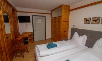 A cozy room with two single beds and wooden furniture. There is a television, a desk, and wall decorations.