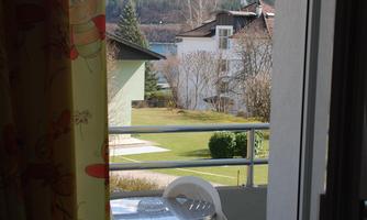 A balcony with a small table and a chair. In the background, mountains and a clear sky can be seen.