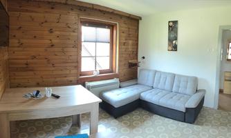 A cozy living space with wood paneling and a large sofa. A table and a television are also available.