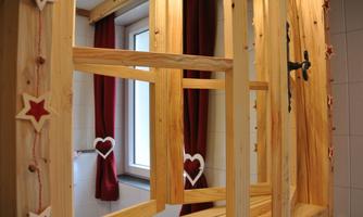 A wooden frame with decorative elements stands in front of a window with red curtains. The window decoration features heart-shaped and star-shaped details.