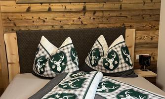 A cozy bedroom with wood paneling and a large window image of a mountain landscape. The duvet and pillows are designed in a traditional style with deer motifs.