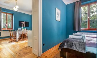 A stylish room with blue walls and wooden flooring. It features a bed and a dining area with chairs.