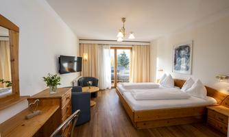 A cozy room with two single beds and a balcony. The decor is modern and bright, with wooden details and a television.