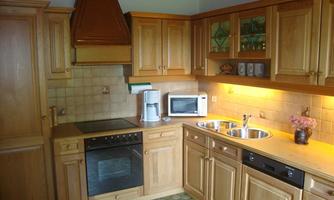 A cozy kitchen made of light wood with modern appliances. On the countertop, there is a microwave and a small flower vase.