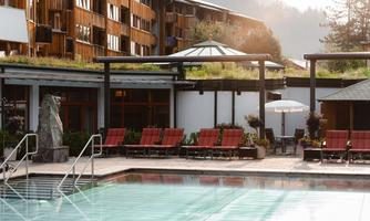 A beautiful outdoor pool with red loungers, surrounded by a modern building. In the background, gentle hills and trees can be seen.