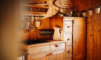 A cozy kitchen with wooden shelves and a wooden cabinet. On the countertop, there is a white kettle and various kitchen appliances.