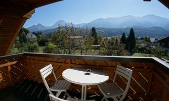 A cozy balcony with a round table and two chairs. In the background, mountain landscapes can be seen under a clear blue sky.