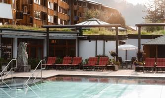 A beautiful outdoor pool with loungers and a modern building in the background. The surroundings are quiet and surrounded by trees.