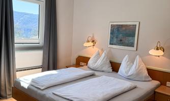 A bright bedroom with a double bed and two pillows. The room has large windows and a pleasant atmosphere.
