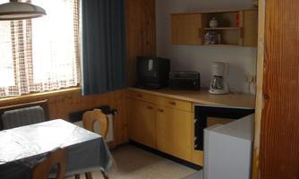 A cozy kitchen with a table, chairs, and wooden kitchen cabinets. On the wall, there is a television and a coffee maker.