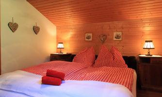 A cozy bedroom with a double bed and checkered bedding. The walls are made of wood, and there are stylish lamps as well as decorative hearts on the wall.