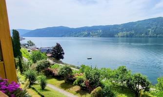 A tranquil lake with green shore areas and gentle hills in the background. The sun is shining and the sky is clear.