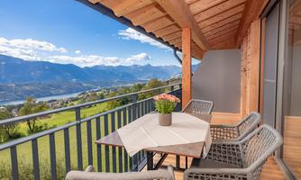 A cozy balcony with a view of the mountains and a river. There is a table with a flower and comfortable chairs.