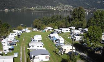 A campsite by the water with many RVs and tents. Surrounded by green nature and mountains in the background.