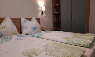 A bright bedroom with two single beds and colorful bedspreads. In the background, there is a wardrobe and a wall lamp gently illuminates the room.