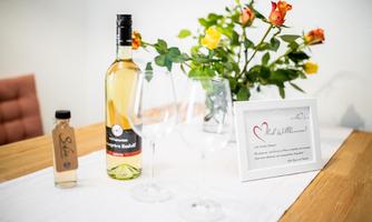 An elegant table with a bottle of wine, two glasses, and a decorative vase with roses. Additionally, a stylish card with a heartfelt message is ready.