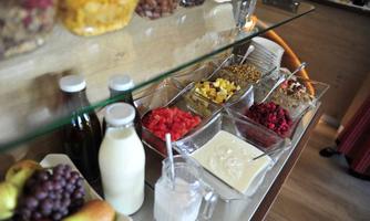 A selection of fresh fruit, yogurt, and muesli in jars. In the foreground are milk and grapes.