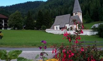 A picturesque church surrounded by colorful flowers and green meadows. In the background, gentle hills rise and a clear blue sky.