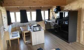 A bright, modern living room with an open kitchen. Large windows let in plenty of light and offer a view of the surroundings.