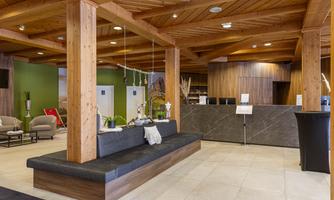 A modern hotel lobby with wooden elements and elegant seating areas. The reception desk is clearly visible and designed in a friendly manner.