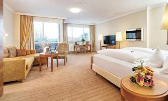 A modern hotel room with a large bed, a cozy seating area, and plenty of natural light. The windows offer a view of the surroundings.