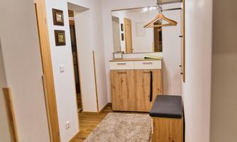 A narrow hallway with wooden furniture and a large mirror. Next to the wall, there is a bench with a carpet in front of it.