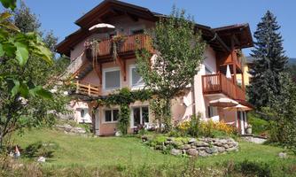A charming house with several balconies, surrounded by trees and green grass. The sky is clear and sunny.