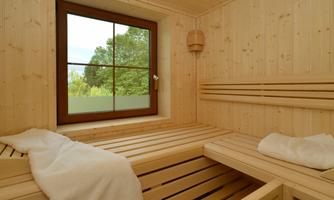 A cozy wooden sauna with benches and a window overlooking nature. Soft towels are ready for relaxation.